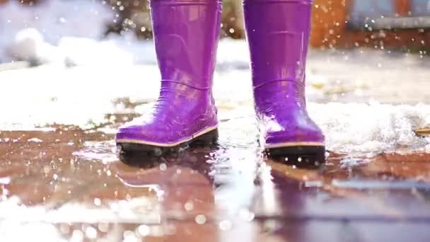Child jumps on puddles in rubber boots at sunset lights in spring time - 映像、動画