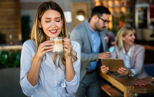 Portrait of happy young successful business woman drinking coffee in a break. In the background, her colleagues - Zdjęcie, obraz