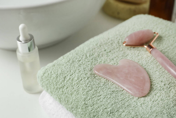 Rose quartz gua sha tool and natural face roller on towel in bathroom, closeup - Foto, Imagen