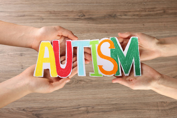 Women holding word Autism made of paper on wooden background, top view - 写真・画像