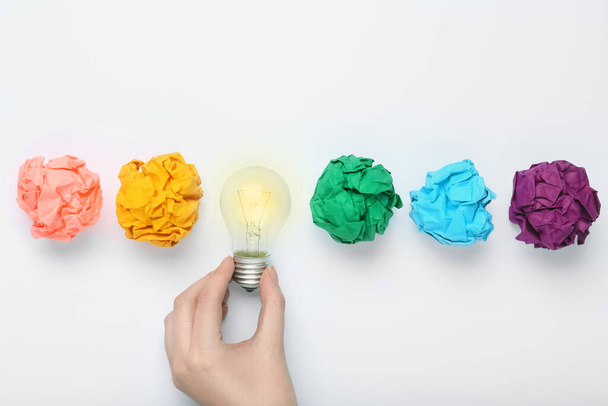 Woman holding lightbulb among colorful paper balls on white background, top view. Idea concept - Foto, Imagen