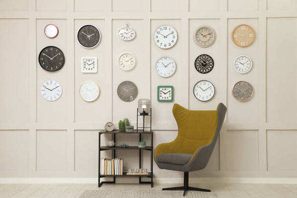 Armchair, console table and many different clocks hanging on white wall in room - Foto, Bild