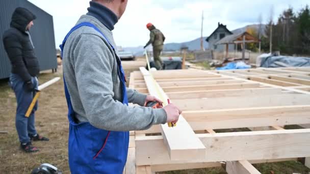 Man worker building wooden frame house on pile foundation. - Video