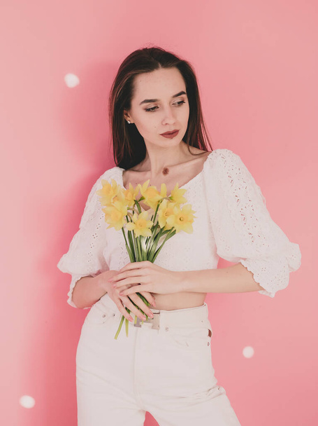 Woman model appearance holds in her hands yellow flowers on a pink background - Fotoğraf, Görsel