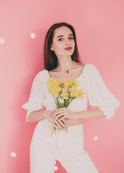 Kobieta model wygląd trzyma w dłoniach żółte kwiaty na różowym tle - Zdjęcie, obraz