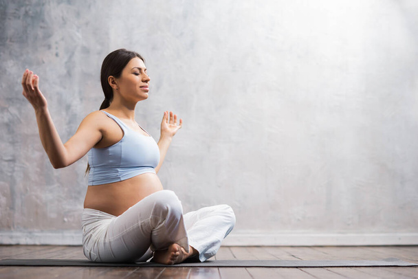 Jovem grávida fazendo exercícios de ioga e meditando em casa. Cuidados de saúde, atenção plena, relaxamento e conceito de bem-estar. - Foto, Imagem