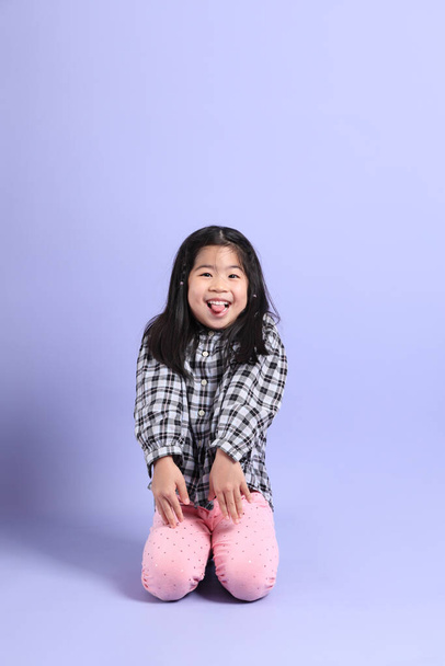 The young Asian gril sitting on the purple background. - Fotografie, Obrázek