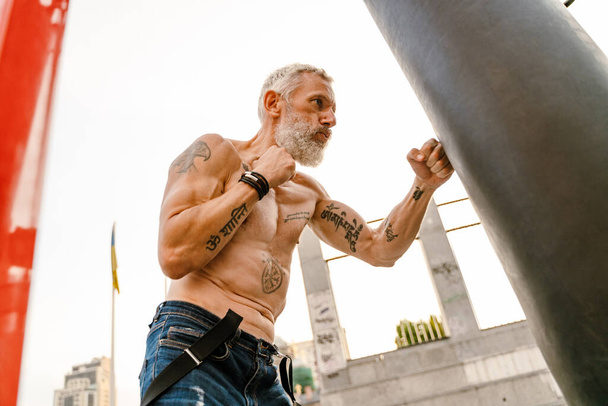 Shirtless mature man with tattoo boxing working out on sports ground outdoors - Photo, image