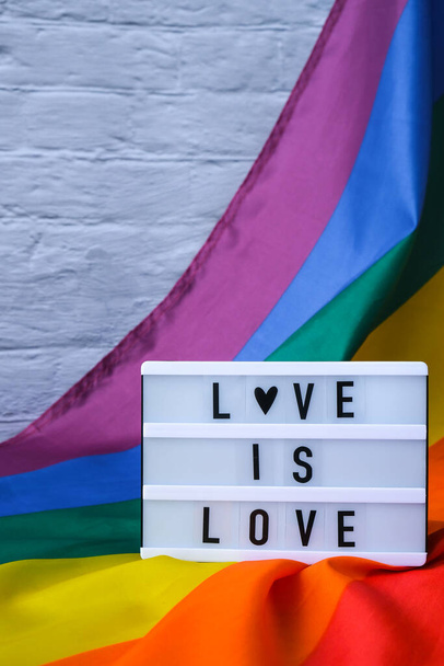 Rainbow flag with lightbox and text LOVE IS LOVE. Rainbow lgbtq flag made from silk material. Symbol of LGBTQ pride month. Equal rights. Peace and freedom - Valokuva, kuva