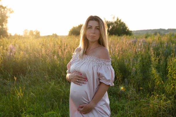 τρυφερό πορτρέτο εγκυμοσύνης στο ηλιοβασίλεμα. Περιμένοντας η μητέρα να είναι έξω με ροζ φόρεμα. Όμορφη τρυφερή φωτογραφία διάθεση της εγκυμοσύνης - Φωτογραφία, εικόνα