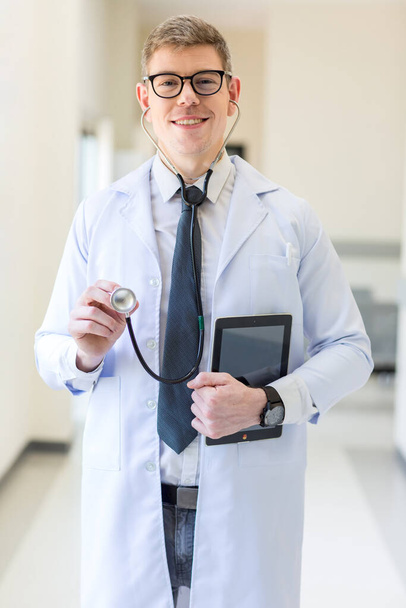 Doctor holding stethoscope at hospital. Friendly male doctor dressed in uniform holding stethoscope. Doctor in a dressing gown with a stethoscope examination in the hands. - Foto, immagini