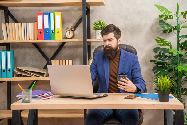 confident bearded boss study online on laptop hold coffee in the office, check email - Фото, изображение