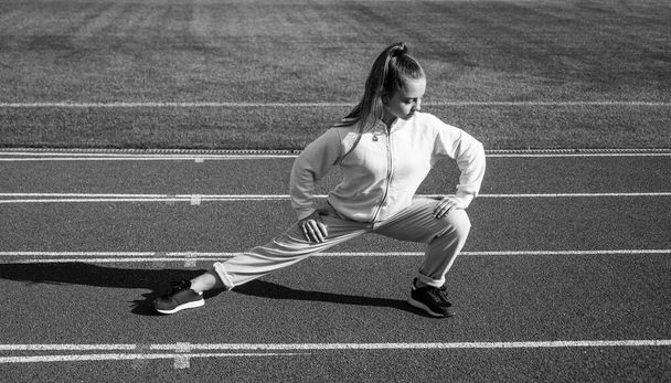 teen girl warming up on stadium. kid in sportswear stretching. child do exercise on racing track. healthy childhood. workout on fresh air outdoor. confident runner. flexible body - Foto, afbeelding
