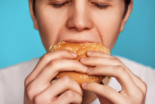 おいしいハンバーガーを持っている非常に空腹の若者 - 写真・画像
