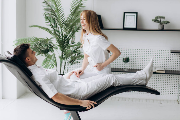 Beyaz önlüklü iki genç dişçi hastanın koltuğunda oynaşıyor. - Fotoğraf, Görsel