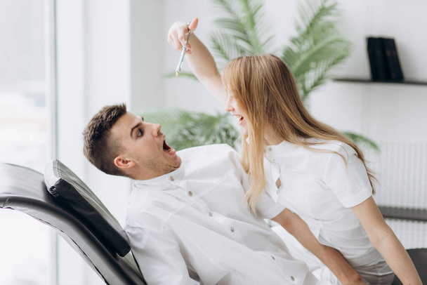 Two young dentists in white coats are fooling around in the patient's chair - Foto, Bild