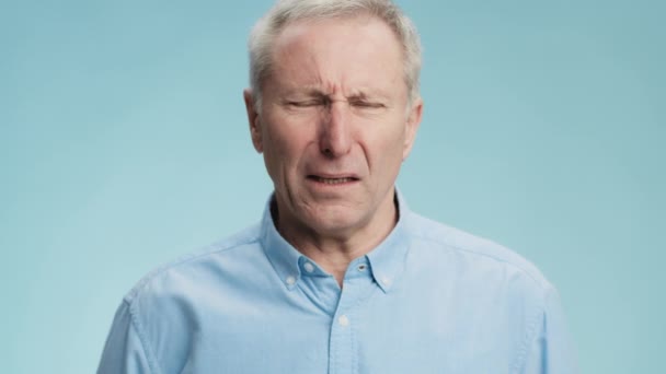 Walgelijk gevoel. Emotionele grijze harige senior man die zich onaangenaam voelt geur, fronsend gezicht en kokhalzende, blauwe achtergrond - Video