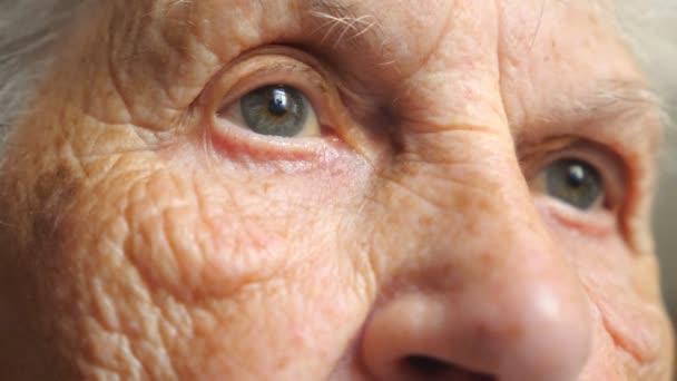 Egy idős nő portréja, amint töpreng valamin. Közelkép a ráncos női arcról. Nagymama nyugodtan néz a távolba, szomorú vagy magányos érzelmeket mutat. Részlet nézet Lassú mozgás - Felvétel, videó