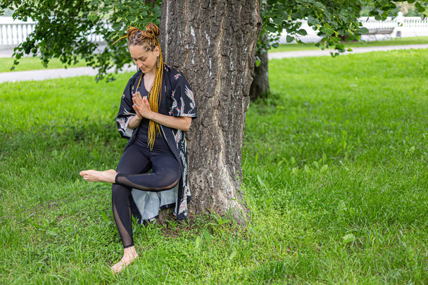 Woman yogi with dreadlocks stretching doing practicing pose on green grass lawn. Relaxing in the morning. Fitness instructor coach showing exercises  - Zdjęcie, obraz