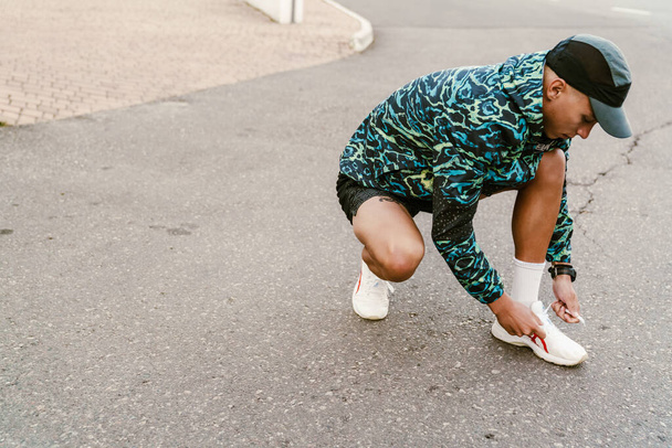 Young white man in sportswear tying his shoelaces during workout outdoors - Fotoğraf, Görsel