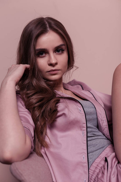 Pretty young woman in pink nightwear with pajamas sits in chair near pink wall - Foto, Imagem
