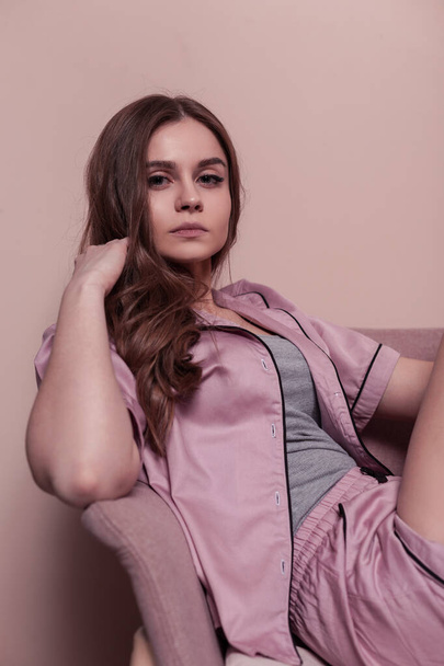 ファッション若いです女性でかなり顔でピンクのナイトウェアパジャマ服はピンクの壁の近くの椅子に座っている - 写真・画像