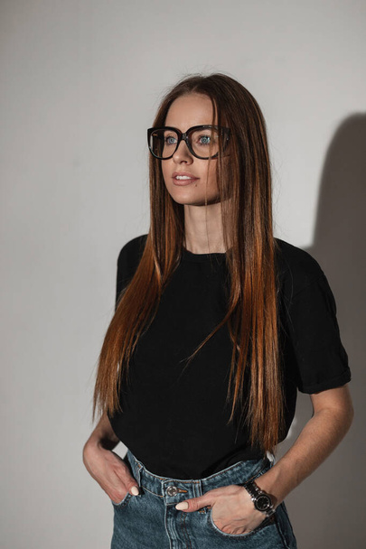 жінка з вінтажними окулярами в чорній стильній футболці макет стоїть в студії
. - Фото, зображення