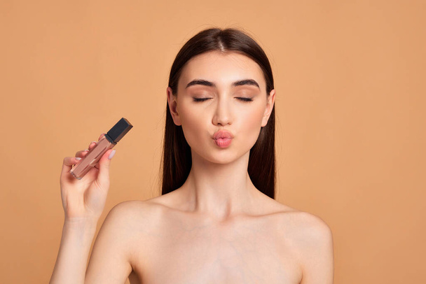 woman with pouted lips holding nude lip gloss - Foto, Imagem