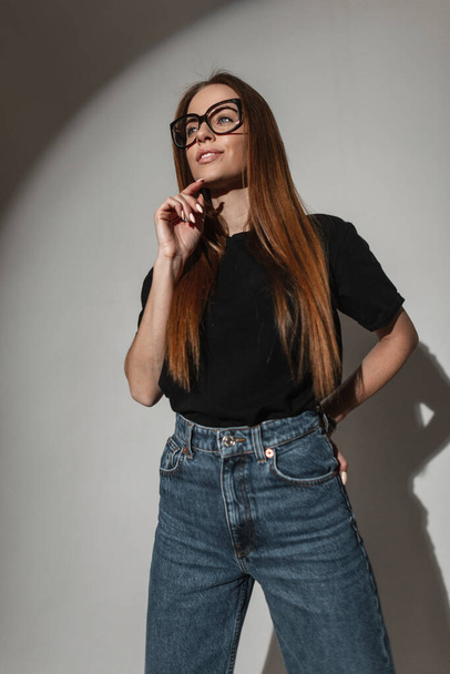 Ευτυχισμένο λαμπερό νεαρή γυναίκα σε μοντέρνα ρούχα με γυαλιά στο στούντιο - Φωτογραφία, εικόνα