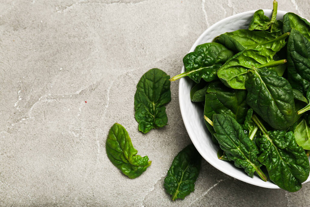 Organic food concept with spinach leaves in a bowl on a cutting board gray background top view copy space - Foto, Imagen