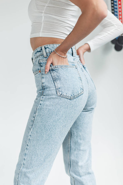 Women's fashion vintage blue jeans. Pretty girl in fashionable denim pants holds her hands in her back pockets. - Foto, Imagen