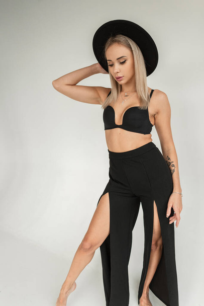 Модель моды Vogue с элегантной черной шляпой в черном лифчике и стильными брюками в помещении - Фото, изображение