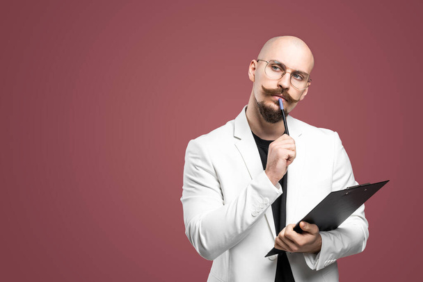 Balded man with mustache and beard in a business suit holding clipboard and pen isolated background.Concept of teacher, psychologist, student, lecturer - 写真・画像