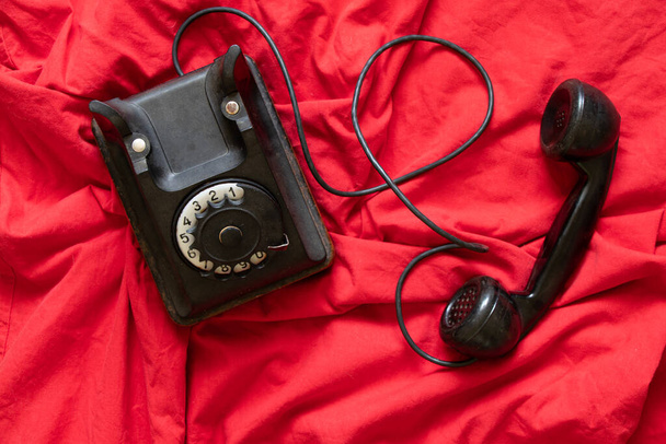 Un vecchio telefono nero vintage poggia su un panno rosso, un telefono vintage del passato - Foto, immagini