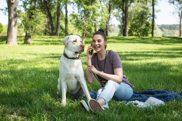 Young beautiful woman in the park with her pet dog white Labrador Retriever that she adopt from the pet shelter to give him good life and love. Female animal lover with her adopted puppy having fun. - Foto, afbeelding