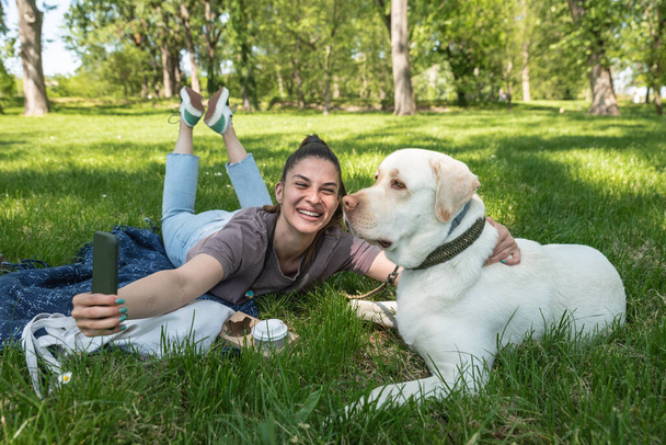 Young beautiful woman in the park with her pet dog white Labrador Retriever that she adopt from the pet shelter to give him good life and love. Female animal lover with her adopted puppy having fun. - Photo, Image