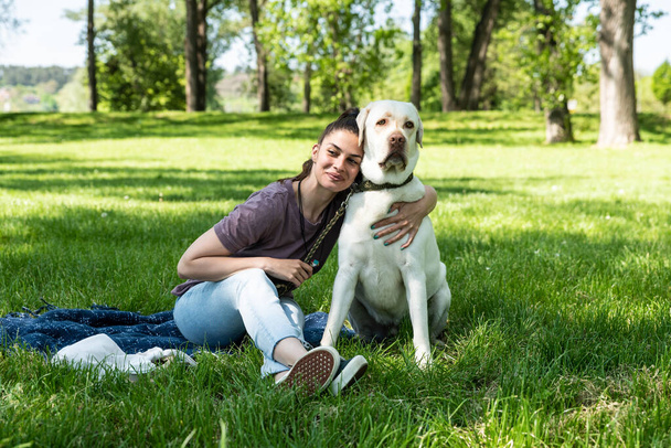 Young beautiful woman in the park with her pet dog white Labrador Retriever that she adopt from the pet shelter to give him good life and love. Female animal lover with her adopted puppy having fun. - Fotoğraf, Görsel