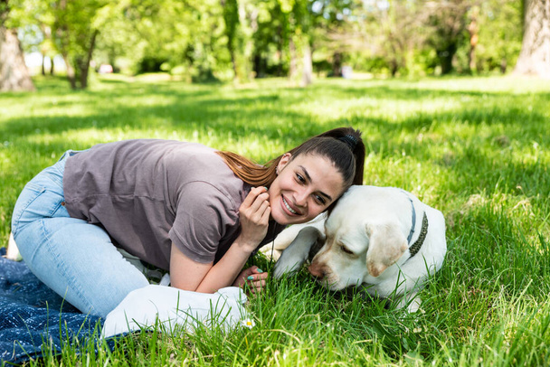 Young beautiful woman in the park with her pet dog white Labrador Retriever that she adopt from the pet shelter to give him good life and love. Female animal lover with her adopted puppy having fun. - Zdjęcie, obraz