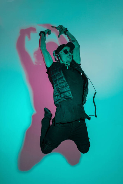 Δροσερός χορευτής με μαύρα ρούχα χορεύει σε έγχρωμο στούντιο με κυάνιο και ροζ φως. Hipster ακούγοντας μουσική και χορό - Φωτογραφία, εικόνα