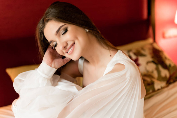 close up portrait of beautiful young woman in white dress posing in bedroom - Foto, Imagem