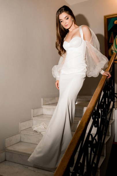 beautiful young woman in a white dress posing on the stairs - Foto, afbeelding
