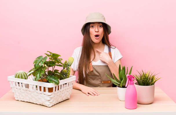 hispanic pretty woman looking shocked and surprised with mouth wide open, pointing to self. plants and gardering concept - Photo, image