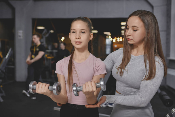 Personal trainer helping her teenage client lifting weights at the gym - Fotó, kép