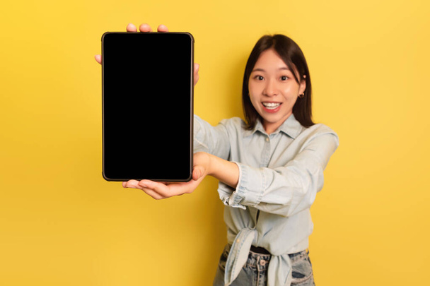 Charmante Asiatin hält digitales Tablet mit leerem Bildschirm in der Hand und empfiehlt neueste mobile Anwendung, Attrappe - Foto, Bild