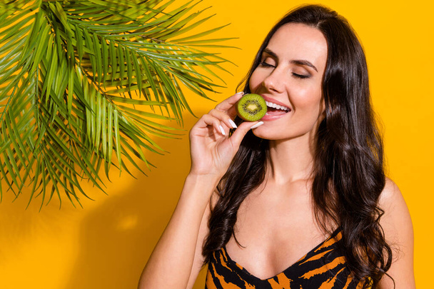 Photo of young pretty woman eat fresh yummy kiwi exotic fruit dream isolated over yellow color background - Foto, afbeelding