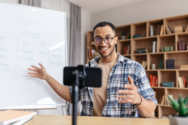Boldog jóképű arab férfi tutor bemutató szabályok az angol és nézi okostelefon otthoni iroda belső - Fotó, kép