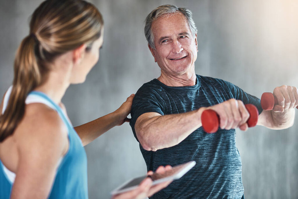 ouder worden, fitter worden, sterker worden. Schot van een oudere man met behulp van gewichten met behulp van een fysiotherapeut. - Foto, afbeelding