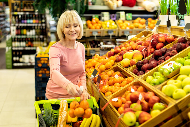 Female customer purchasing at supermarket, choosing fruits - Foto, Imagen