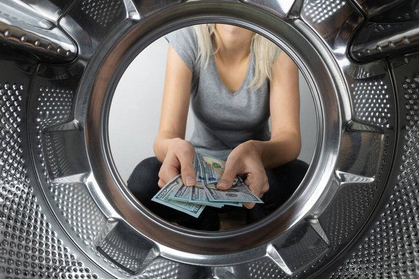 Frauenhände halten Geld in der Nähe der Waschmaschine, ein Foto aus der Trommel der Waschmaschine. Konzept der Zahlung, Geldwäsche. - Foto, Bild
