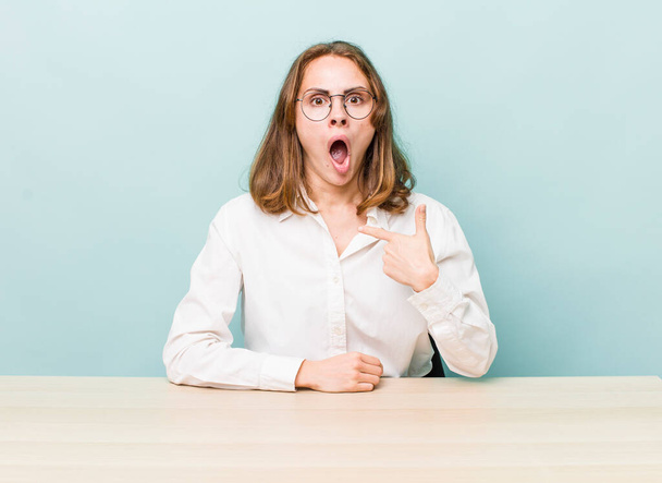 young pretty woman  looking shocked and surprised with mouth wide open, pointing to self. desk and business concept - Foto, Imagem